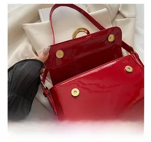Detail view of red patent leather bag showing golden magnetic buckles and glossy finish