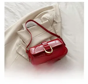 Detail of red patent leather shoulder bag featuring a gold horseshoe buckle accent