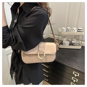 Detail of glossy beige patent leather bag featuring a gold horseshoe buckle on the front