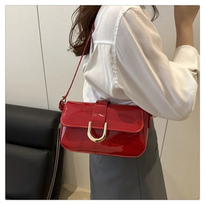 Detail of red patent leather shoulder bag with a polished gold horseshoe buckle clasp