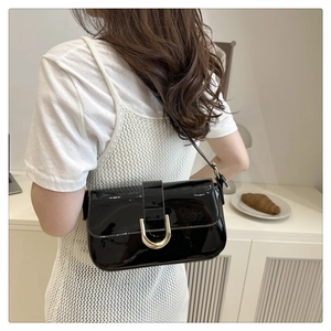 Detail of black patent leather shoulder bag with gold horseshoe buckle worn by a model