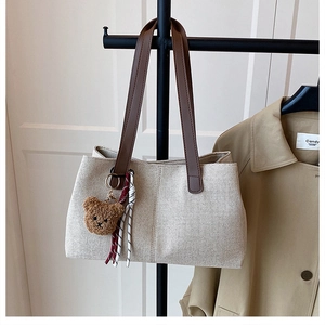 Detail of beige canvas tote with dark brown leather straps and cute bear pendant charm
