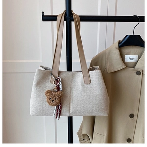 Detail of off-white woven tote bag featuring leather handles and brown teddy bear charm