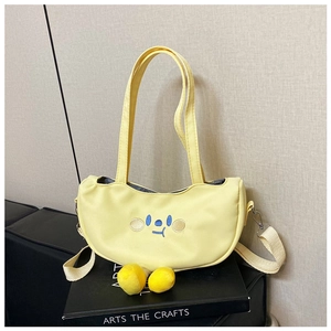 Close-up of yellow canvas half-moon bag with blue cartoon face and plush ball charms