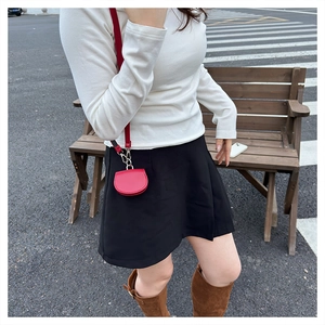 Detailed view of a mini round red leather waist bag with metal buckle on a shoulder strap