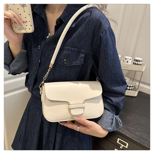 Detail of a minimalist cream crossbody bag featuring a golden chain strap and leather finish