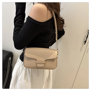 Model wearing a chic beige crossbody bag with gold chain strap on a white background