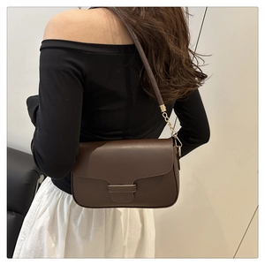 Detail view of a dark brown crossbody flap bag with gold chain strap on female model
