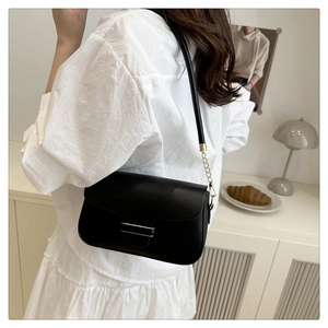 Detail of minimalist black crossbody bag with gold hardware and metal chain strap