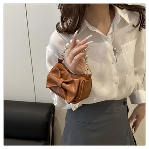 Close-up of caramel brown mini handbag with large bow and elegant faux pearl chain handle