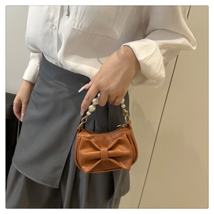 Detail of a brown bow handbag featuring an elegant faux pearl carry handle and gold hardware