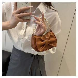 Detail of a brown leather bag with a large bow and elegant pearl handle strap