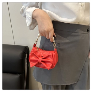Detail of red bow square bag featuring pearl top handle and golden hardware finish