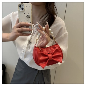 Detail of red square handbag featuring large leather bow and pearl beaded handle