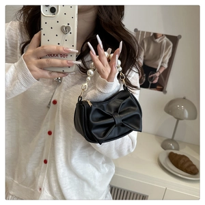 Close-up of black bow handbag featuring elegant large pearl handle and smooth PU leather