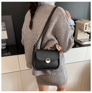 Chic black saddle bag with dual-tone ring buckle and decorative scarf on model