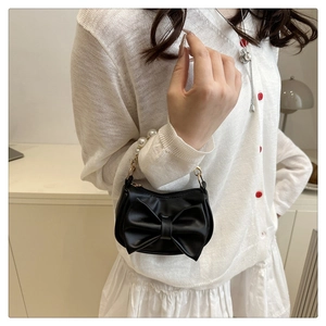 Detail of a black PU leather mini handbag with a large bow and pearl handle on a model
