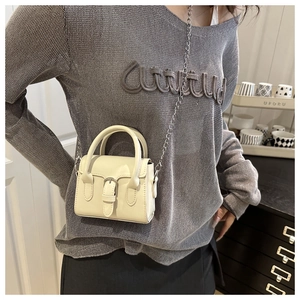 Mini cream leather bag with metal chain strap worn by a model in a cozy setting