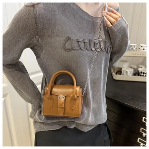 Detail of caramel brown mini handbag with metal chain strap and top handle on model