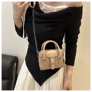 Detail of vintage beige crossbody bag with silver chain strap on model in stylish indoor setting