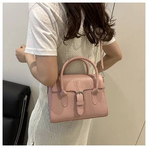 Rear view of model wearing a pale pink crossbody handbag with buckle detail and dual handles