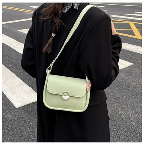 Street style view of a light green crossbody bag featuring a decorative pink silk scarf