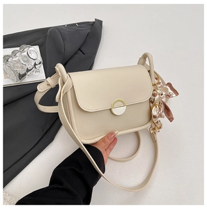 Detail of cream shoulder bag with golden ring lock and floral scarf decoration