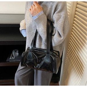 Close-up of a black glossy wrinkled patent leather shoulder bag on a model wearing grey