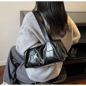 Detail of a black glossy wrinkled leather baguette bag on model in grey sweater