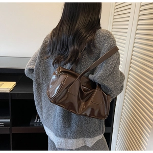 Close-up of dark brown patent leather shoulder bag styled with a grey knitted sweater