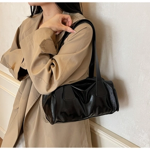 Close-up of black glossy patent leather shoulder bag with fine stitching on model