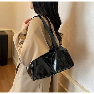 Close-up of a black glossy baguette shoulder bag with stylish side pleats and double straps