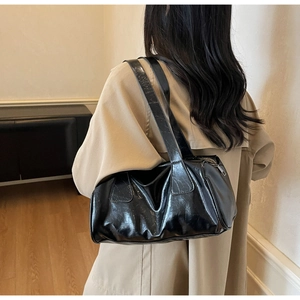 Close-up of glossy black shoulder bag with oil wax leather texture and sleek metal zipper