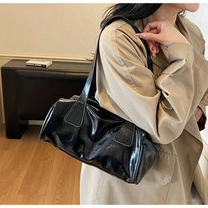 Detail of black glossy vintage baguette bag featuring retro wrinkled texture and long handle