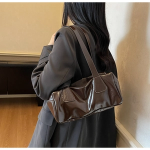 Detailed view of deep brown glossy patent leather shoulder bag with wide strap on model