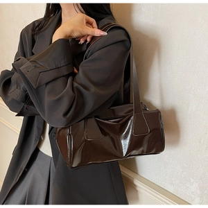 Detailed view of a dark brown glossy baguette bag worn under the arm with a blazer