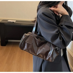 Detail of glossy dark brown leather shoulder bag featuring minimalist baguette silhouette