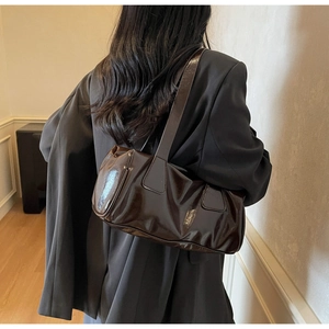 Detail view of glossy dark brown baguette shoulder bag styled on a person in a suit
