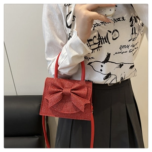 Close-up of red glitter mini bag with oversized bow and chain strap on a model
