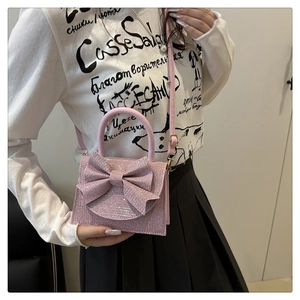 Detailed view of a pink sparkling evening bag with bow detail worn as a crossbody bag