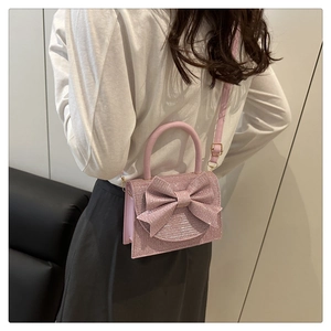 Rear view of model wearing pink glitter crossbody bag with large decorative bow detail
