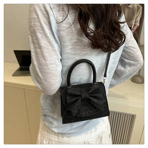Close-up of black glitter bow handbag with gold buckle shown in a lifestyle indoor setting