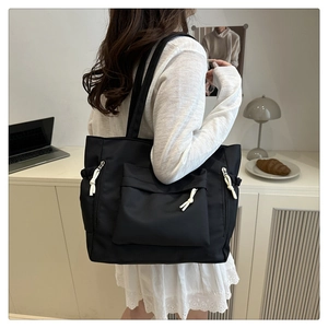 Close-up of black nylon tote bag with white knot zippers worn by model in minimalist room