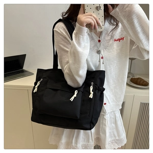 Detail of black nylon tote bag featuring front pocket and side white knotted zippers
