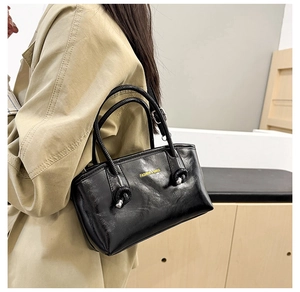 Detail of black glossy tote bag with gold lettering shown on a shoulder strap