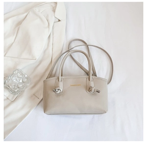 Detail of beige faux leather tote showing gold embossed lettering and metal knot buckle