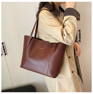 Détail d'un grand cabas en cuir marron avec logo doré porté sur un trench-coat élégant