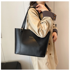 Gros plan d'un cabas noir en cuir PU avec lettrage doré porté sur un trench-coat beige