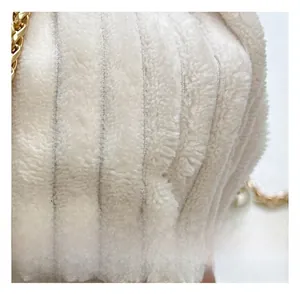 Macro detail of creamy white plush bucket bag with vertical texture and gold chain