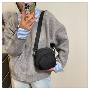 Detail of a lightweight black nylon crossbody round bag with adjustable fabric shoulder strap